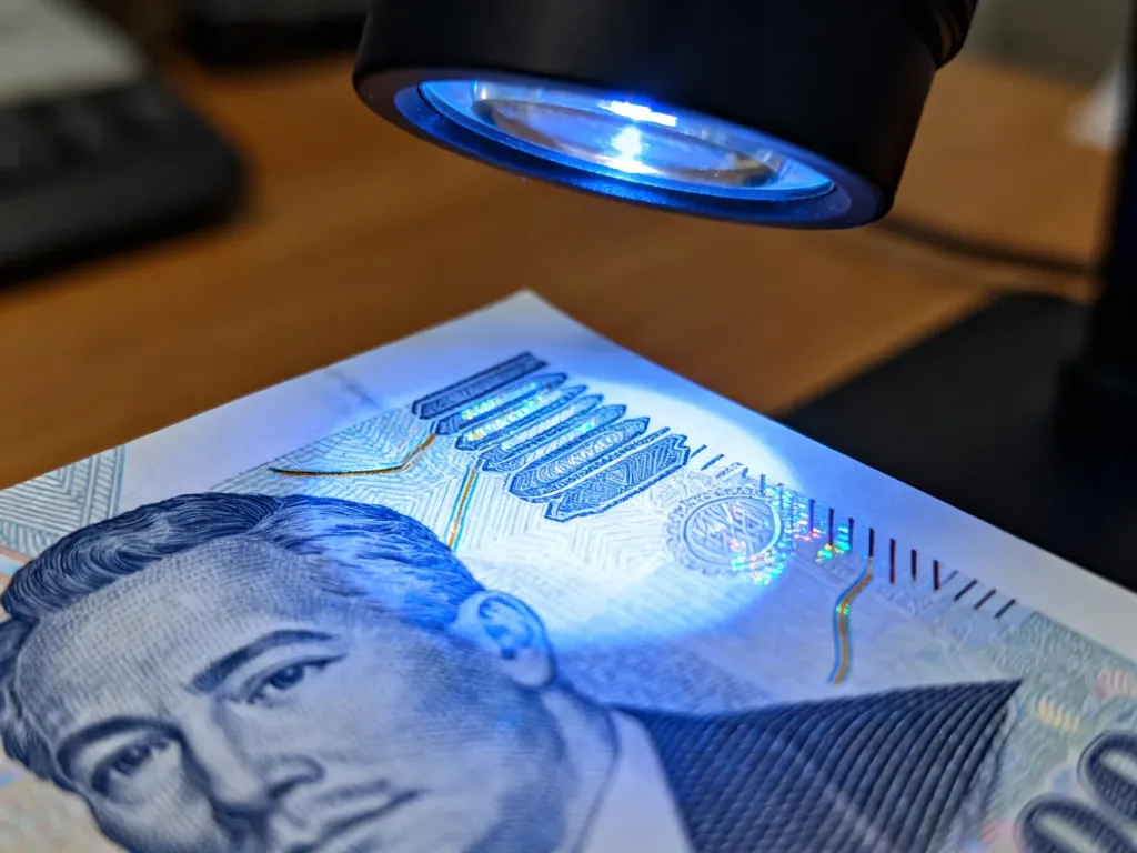 Zbliżenie na zabezpieczenia banknotu 100 zł w świetle UV, ukazujące hologramy i znaki wodne w celu weryfikacji autentyczności.